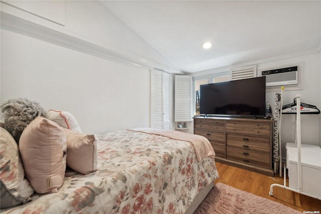 bedroom with light hardwood / wood-style floors, a wall unit AC, and vaulted ceiling