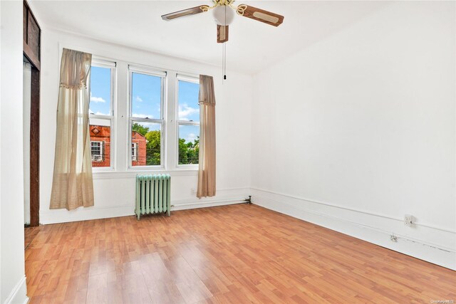 unfurnished room with ceiling fan, radiator heating unit, and light hardwood / wood-style flooring