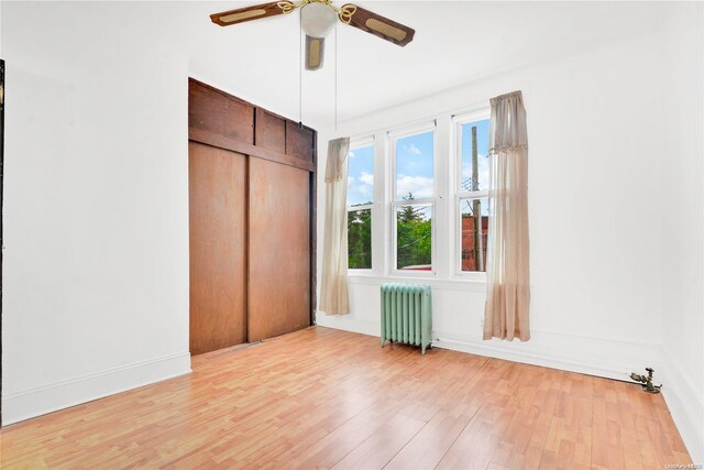 unfurnished bedroom with radiator heating unit, a closet, light hardwood / wood-style floors, and ceiling fan