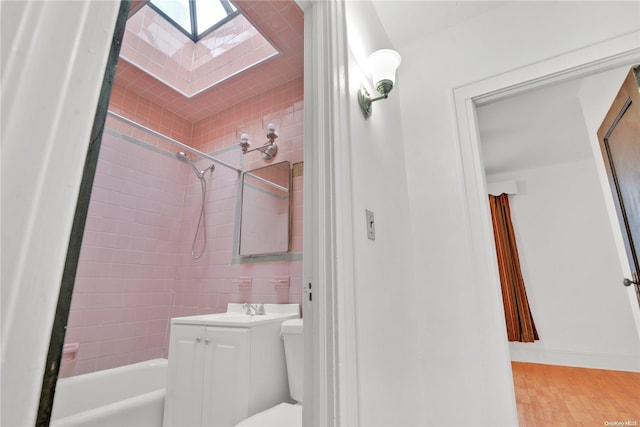 full bathroom featuring a skylight, tiled shower / bath combo, toilet, vanity, and hardwood / wood-style flooring