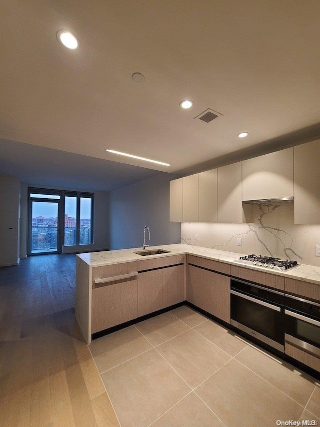 kitchen with white gas stovetop, sink, light hardwood / wood-style flooring, tasteful backsplash, and kitchen peninsula