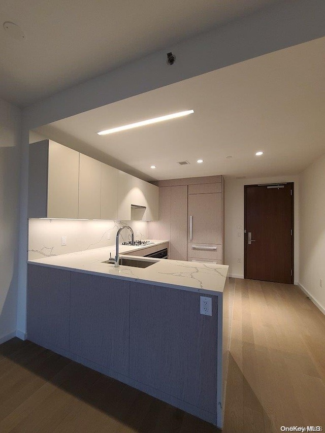 kitchen with sink, kitchen peninsula, tasteful backsplash, dark hardwood / wood-style flooring, and white cabinetry