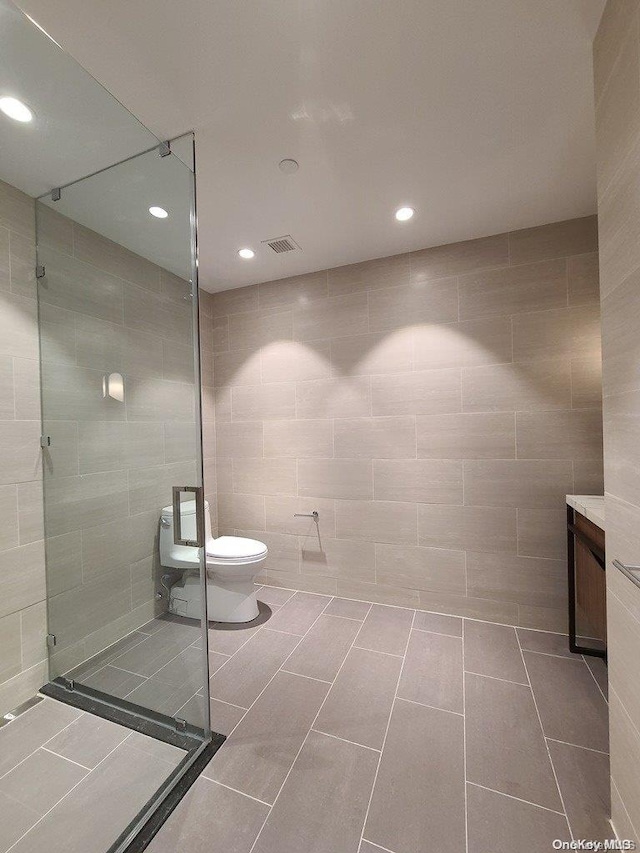 bathroom with tile patterned floors, a shower, toilet, vanity, and tile walls