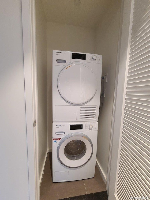 laundry area featuring dark tile patterned flooring and stacked washer / dryer