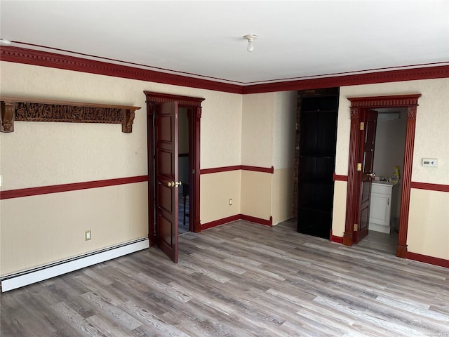 unfurnished room with hardwood / wood-style flooring, baseboard heating, and crown molding