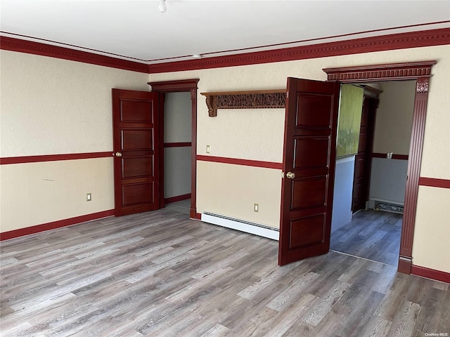 empty room with crown molding, light hardwood / wood-style flooring, and a baseboard heating unit