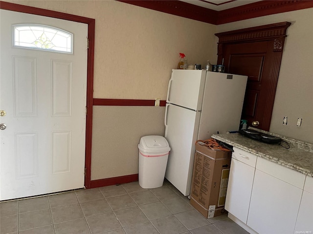 kitchen with white fridge, white cabinetry, crown molding, and light tile patterned floors