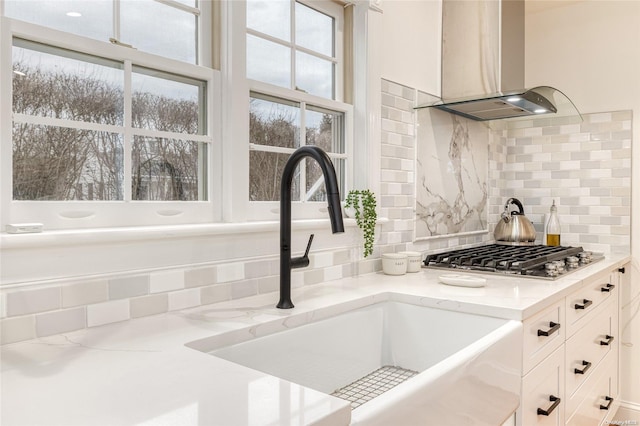 details with decorative backsplash, light stone counters, wall chimney range hood, and sink