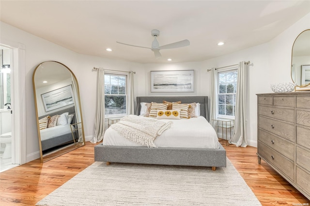 bedroom featuring multiple windows, light hardwood / wood-style floors, ensuite bath, and ceiling fan