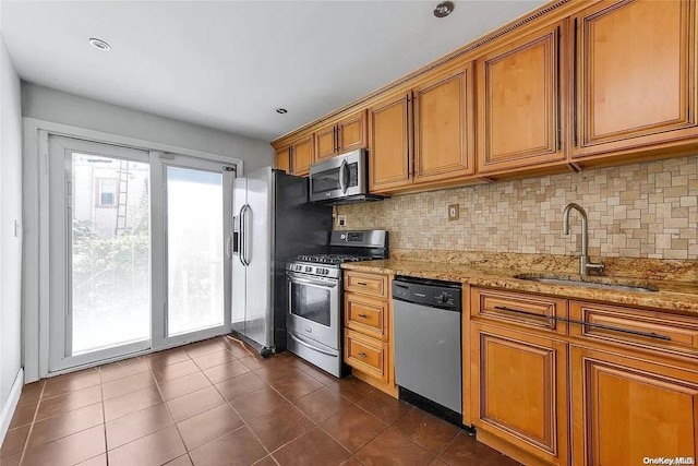 kitchen featuring sink, decorative backsplash, dark tile patterned floors, light stone counters, and stainless steel appliances