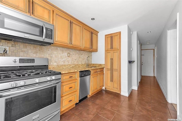 kitchen featuring light stone countertops, sink, stainless steel appliances, backsplash, and dark tile patterned flooring