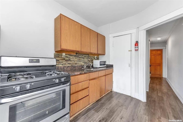 kitchen with sink, stainless steel gas range, dark hardwood / wood-style floors, dark stone countertops, and decorative backsplash