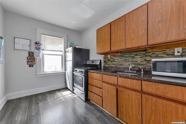 kitchen featuring appliances with stainless steel finishes, tasteful backsplash, dark stone counters, sink, and dark hardwood / wood-style floors