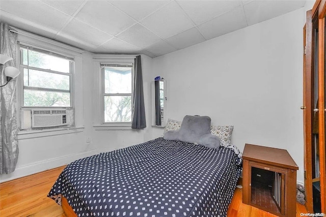 bedroom with hardwood / wood-style flooring, a drop ceiling, cooling unit, and multiple windows