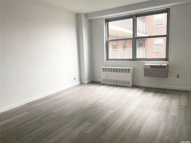 spare room featuring wood-type flooring, radiator, and a wall mounted AC