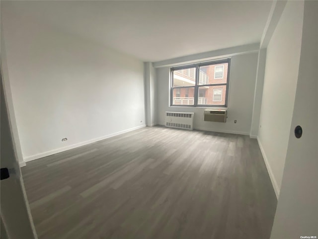 empty room with a wall unit AC, dark hardwood / wood-style flooring, and radiator