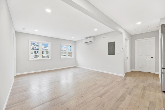 unfurnished room featuring a wall mounted air conditioner, light wood-type flooring, and electric panel