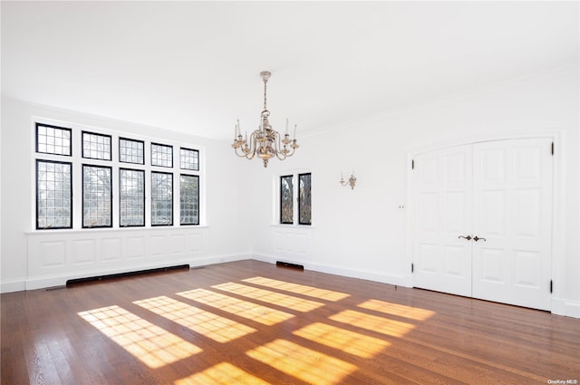 empty room with a notable chandelier, dark hardwood / wood-style floors, and crown molding