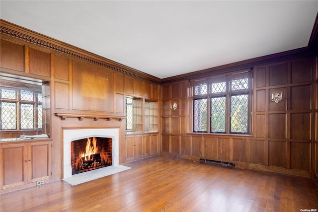 unfurnished living room featuring ornamental molding, light hardwood / wood-style floors, and wooden walls