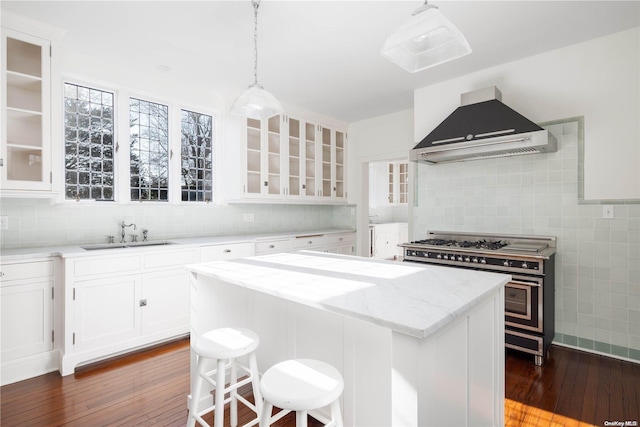 kitchen with sink, wall chimney exhaust hood, a kitchen island, range with two ovens, and white cabinets