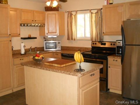 kitchen with light brown cabinetry, ceiling fan, a center island, and stainless steel appliances