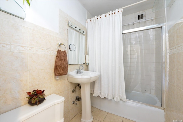 bathroom with tile patterned flooring, toilet, bath / shower combo with glass door, and tile walls