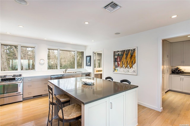 kitchen with a kitchen bar, stainless steel appliances, white cabinetry, light hardwood / wood-style floors, and a kitchen island