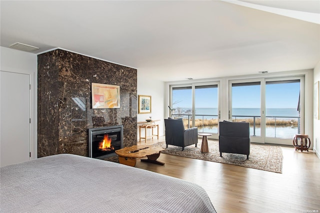 bedroom with a high end fireplace, wood-type flooring, a water view, and access to outside