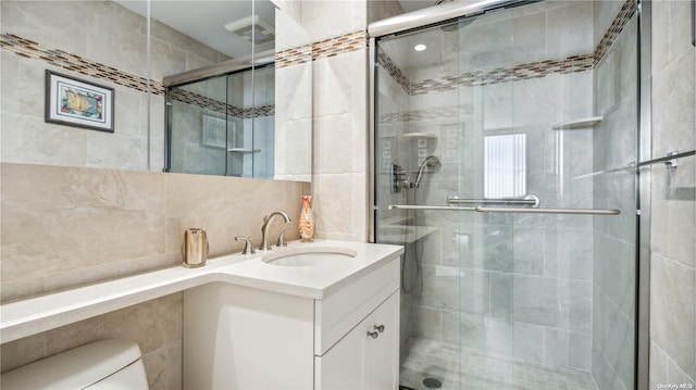 bathroom featuring vanity, toilet, walk in shower, and tile walls