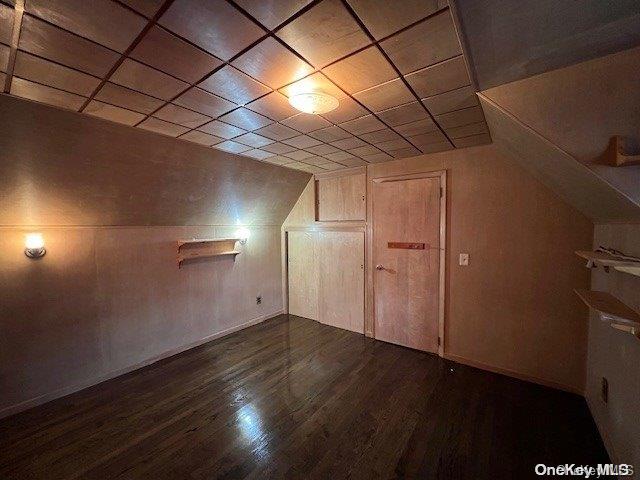 additional living space with wood walls and dark wood-type flooring