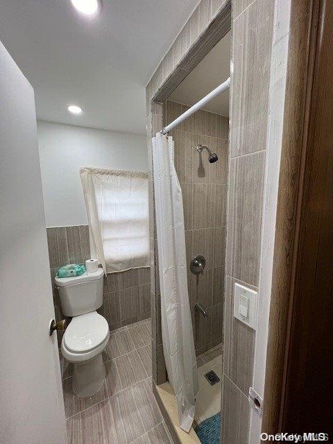 bathroom with curtained shower, toilet, and tile walls