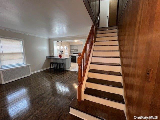 stairway with wood-type flooring, radiator heating unit, and crown molding