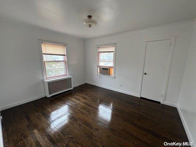 unfurnished room with radiator heating unit, cooling unit, dark wood-type flooring, and plenty of natural light