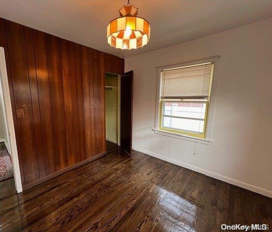 spare room with dark hardwood / wood-style flooring, an inviting chandelier, and wooden walls