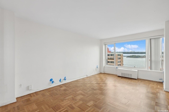 empty room featuring a water view, radiator, and light parquet flooring