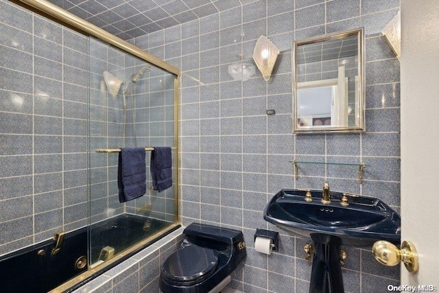 full bathroom featuring backsplash, bath / shower combo with glass door, sink, tile walls, and toilet