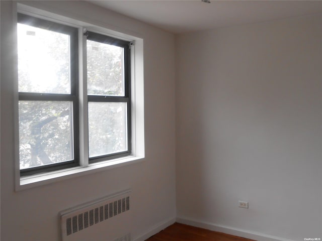 empty room featuring radiator, plenty of natural light, and dark hardwood / wood-style flooring