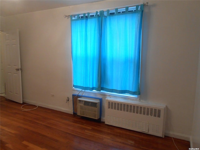 empty room featuring a wall mounted air conditioner, radiator heating unit, and dark wood-type flooring