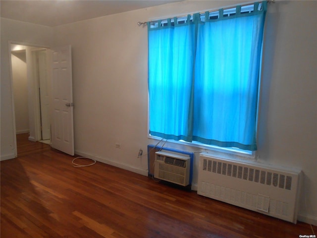 empty room with dark hardwood / wood-style flooring, radiator heating unit, and a wall mounted air conditioner