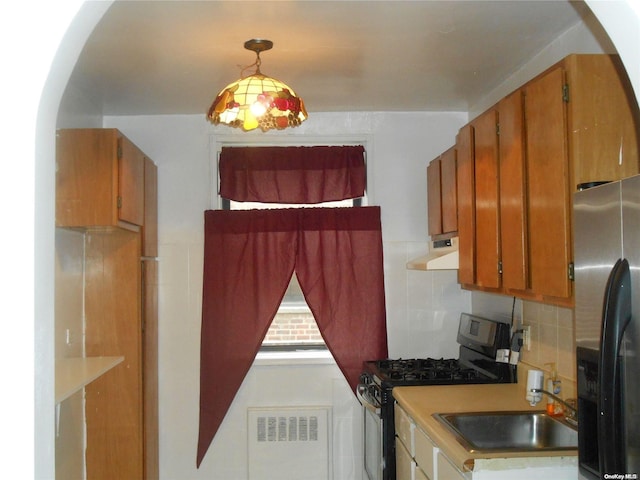 kitchen featuring stainless steel refrigerator with ice dispenser, tasteful backsplash, radiator, black range with gas stovetop, and decorative light fixtures