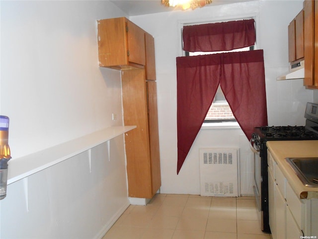 kitchen with radiator heating unit, light tile patterned flooring, and stainless steel gas range