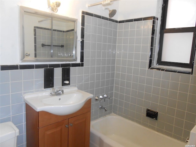 full bathroom with toilet, vanity, tiled shower / bath combo, and tile walls