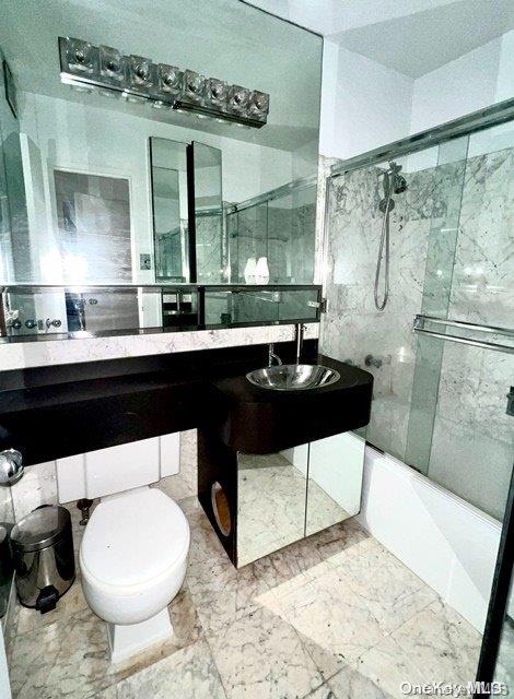 bathroom featuring toilet and bath / shower combo with glass door