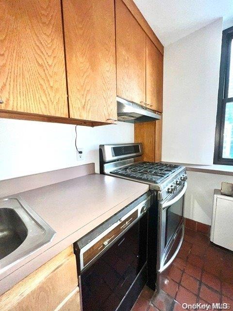 kitchen featuring dishwasher, dark tile patterned flooring, stainless steel gas range oven, and sink