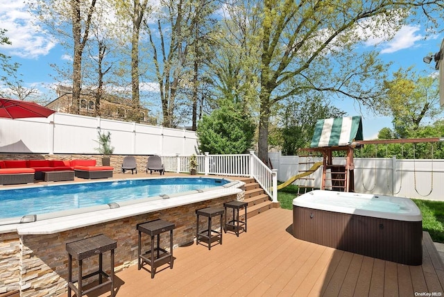 view of pool with outdoor lounge area, a deck, a hot tub, a playground, and a bar