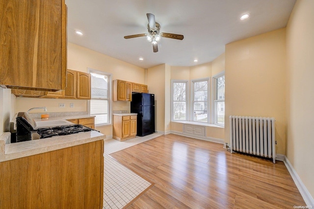 kitchen featuring radiator heating unit, light hardwood / wood-style floors, black fridge, and a wealth of natural light