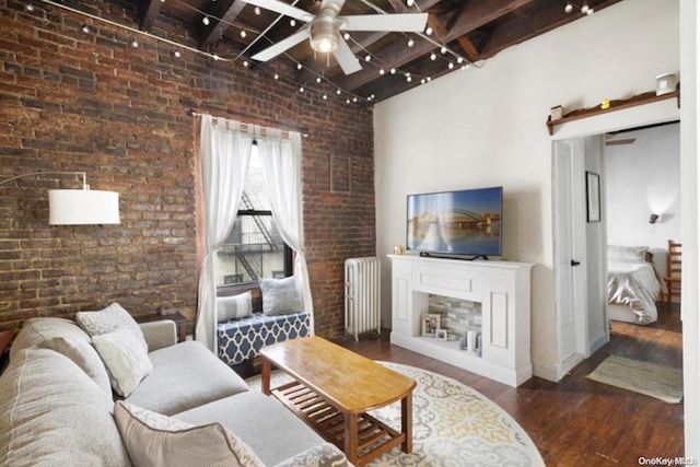 living room with dark wood-type flooring, a high ceiling, ceiling fan, radiator heating unit, and brick wall