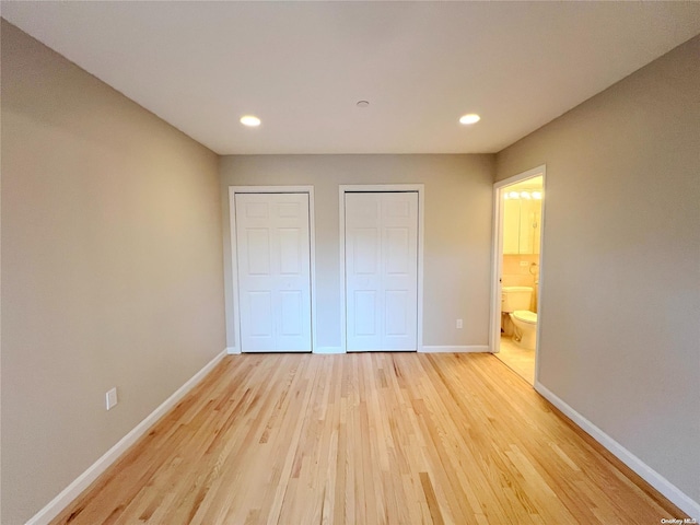 unfurnished bedroom featuring two closets, connected bathroom, and light hardwood / wood-style flooring