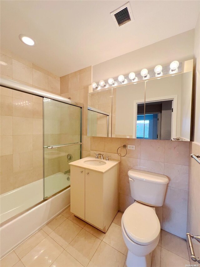 full bathroom with vanity, shower / bath combination with glass door, tile patterned floors, toilet, and tile walls