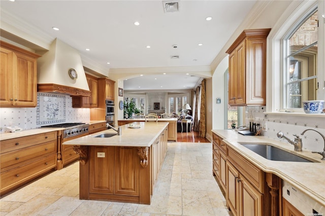 kitchen with premium range hood, a kitchen island with sink, sink, and crown molding